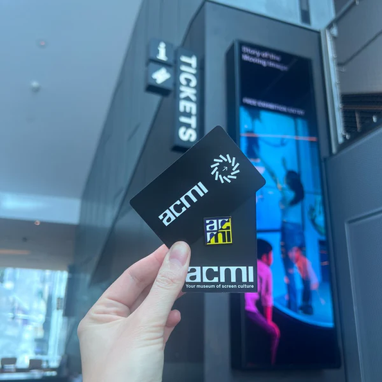 A hand holding an ACMI Member card with exclusive enamel pin