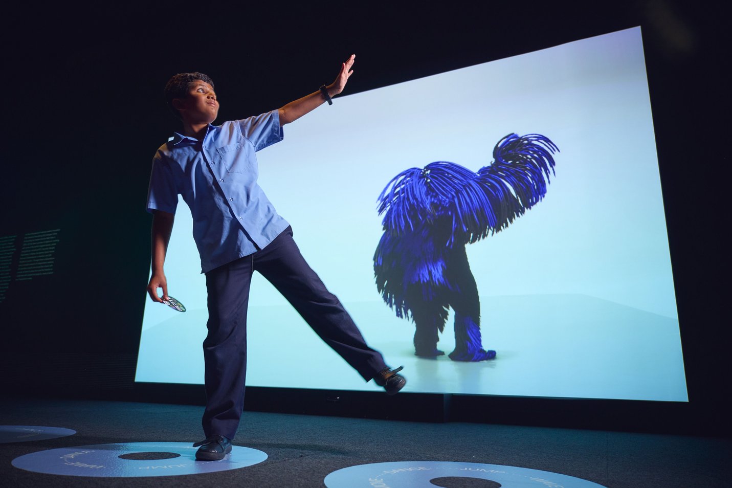 School boy poses in front of interactive screen with shaggy creature responding to his movements