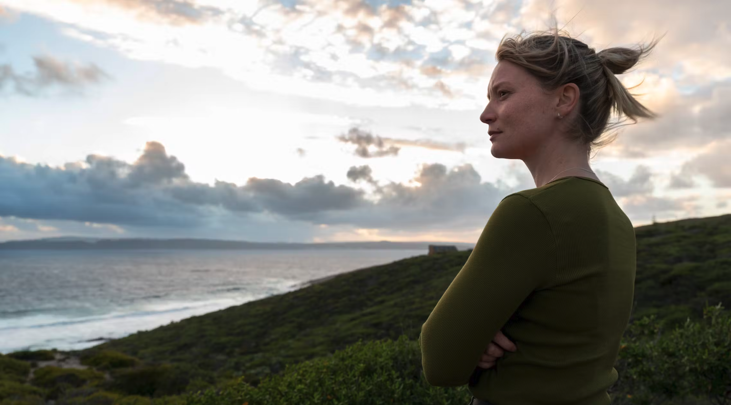 Woman dressed in olive green looks out onto the ocean