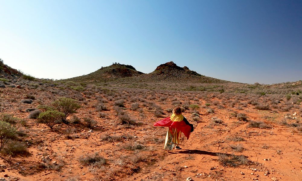 Kaylene Whiskey carrying an Aboriginal flag in a desert landscape