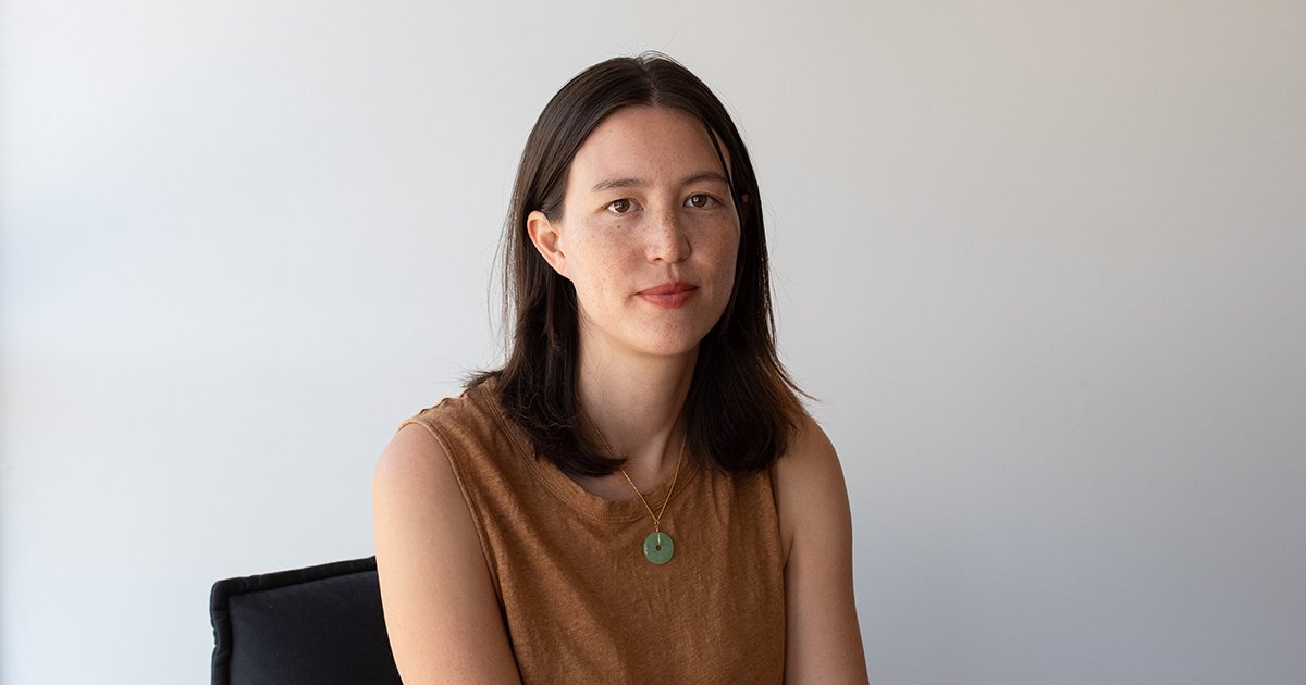 A portrait of a young woman with dark hair, wearing a brown top.