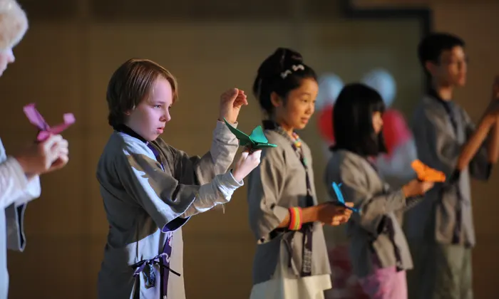 Children stand in line holding paper planes