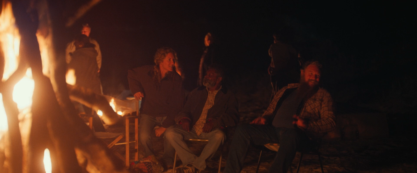 People dance together in the night around a large fire on the beach