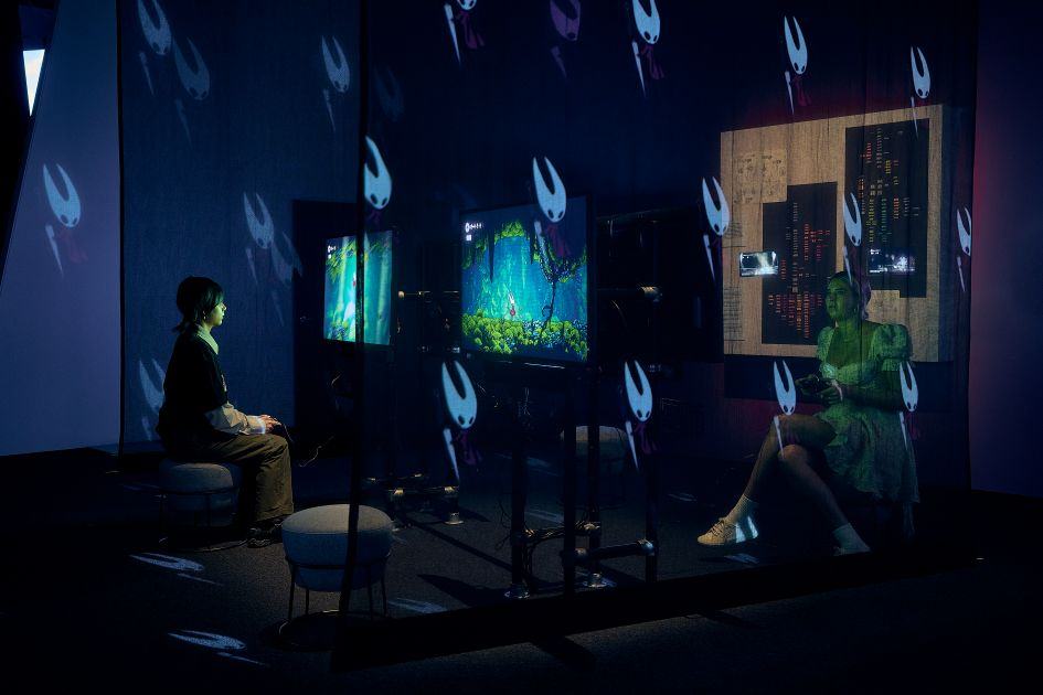 Two girls playing videogames with Hollow Knight Silksong projected images
