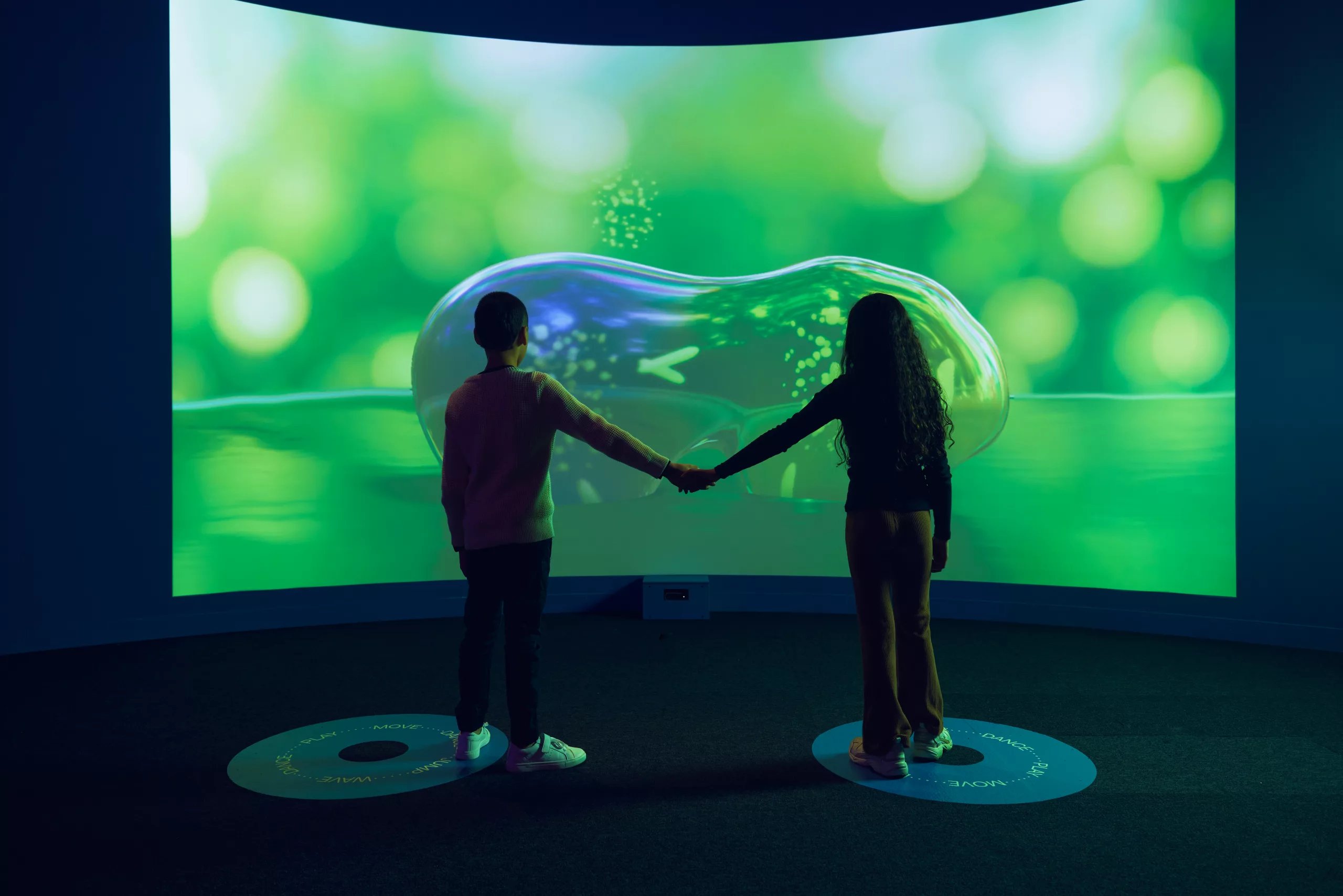 Children hold hands as they interact with bubble like interactive artwork