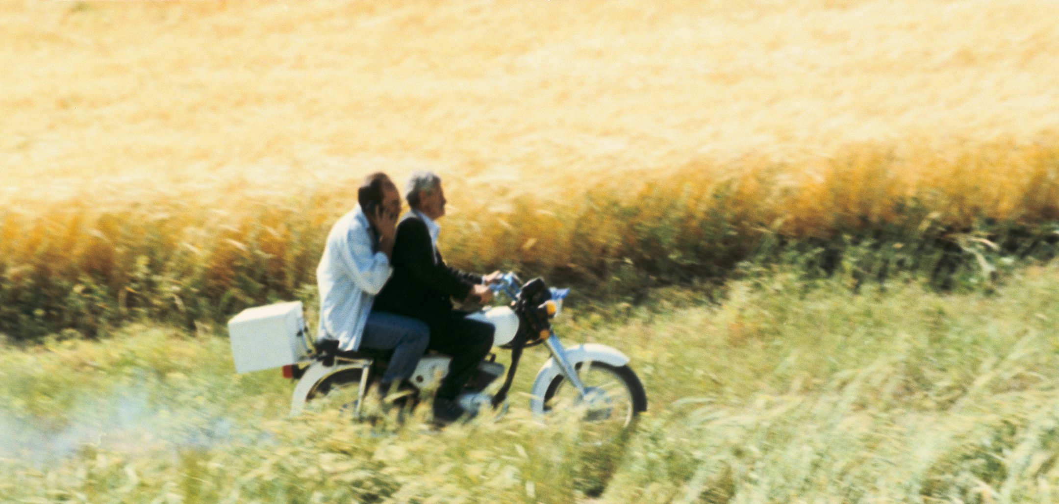 Still of Behzad Dorani and the doctor on a motorbike in a still from 'The Wind Will Carry Us' (1999, Copyright MK2)