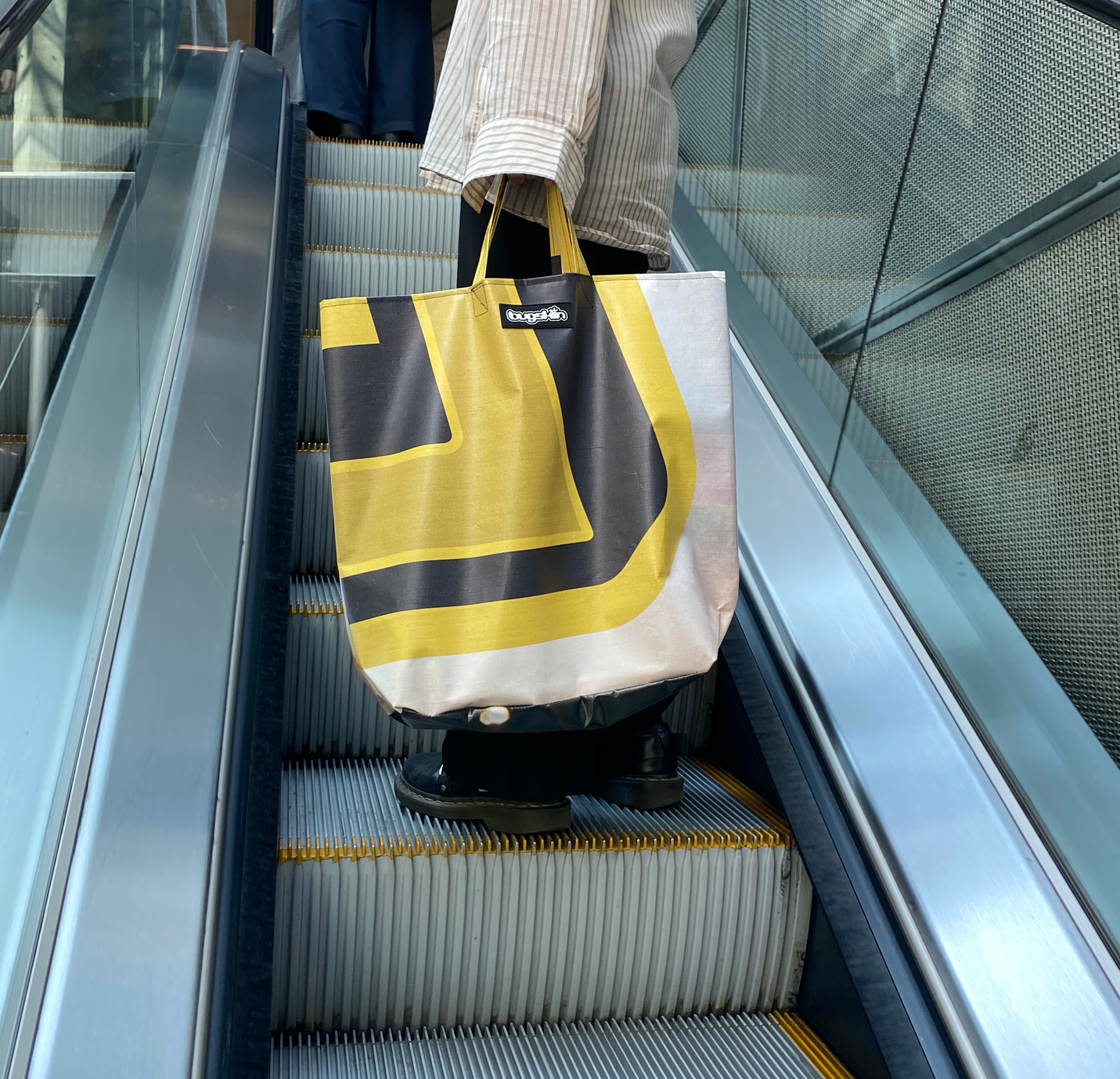 A person holding a Bugskin bag while going up an escalator
