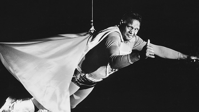 Zac Martin in a superhero costume being held up by a wire in a still from 'Basically Black' (1973)