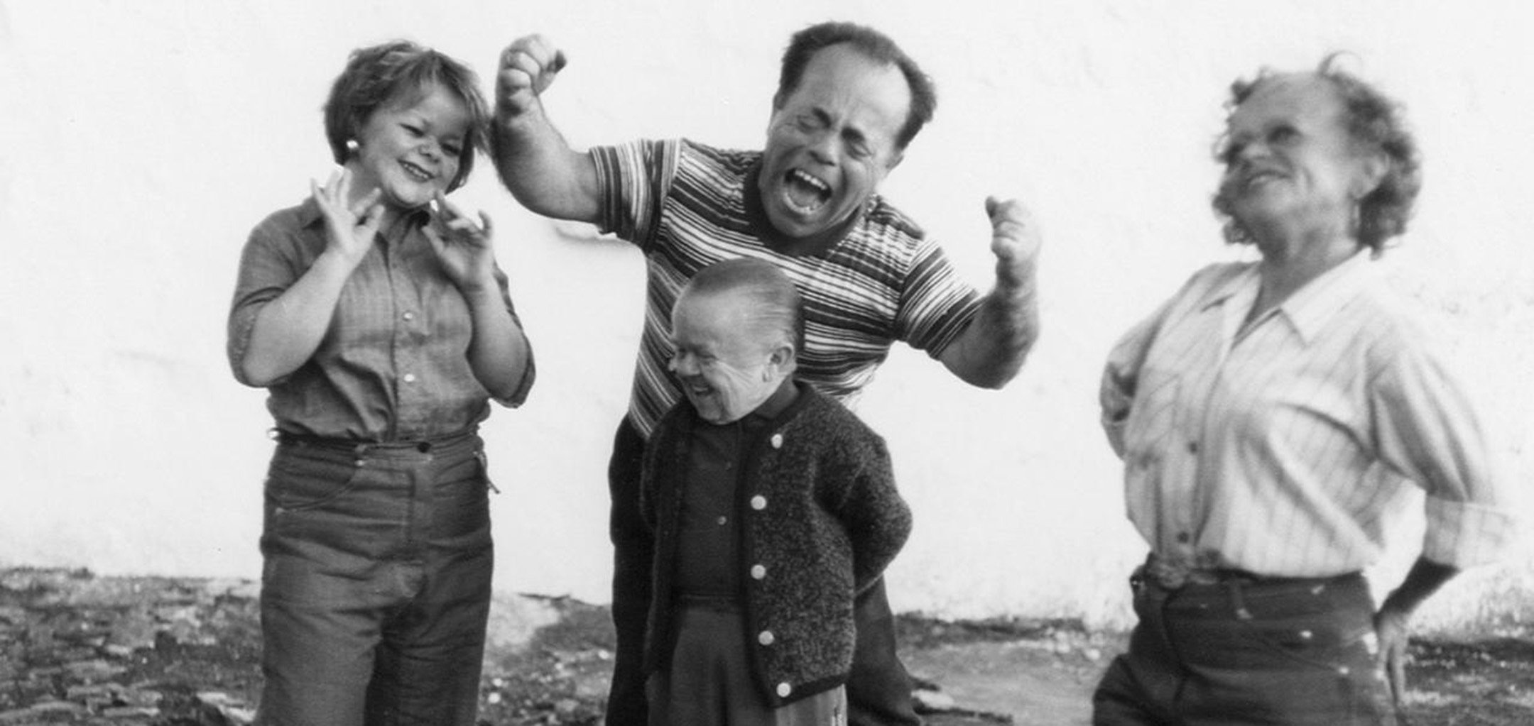A black and white photo of 4 cast members from Even Dwarfs Started Small (1970).
Helmut Döring stands in the centre with his arms behind his back, smiling, while his cast members are also laughing and smiling around him.