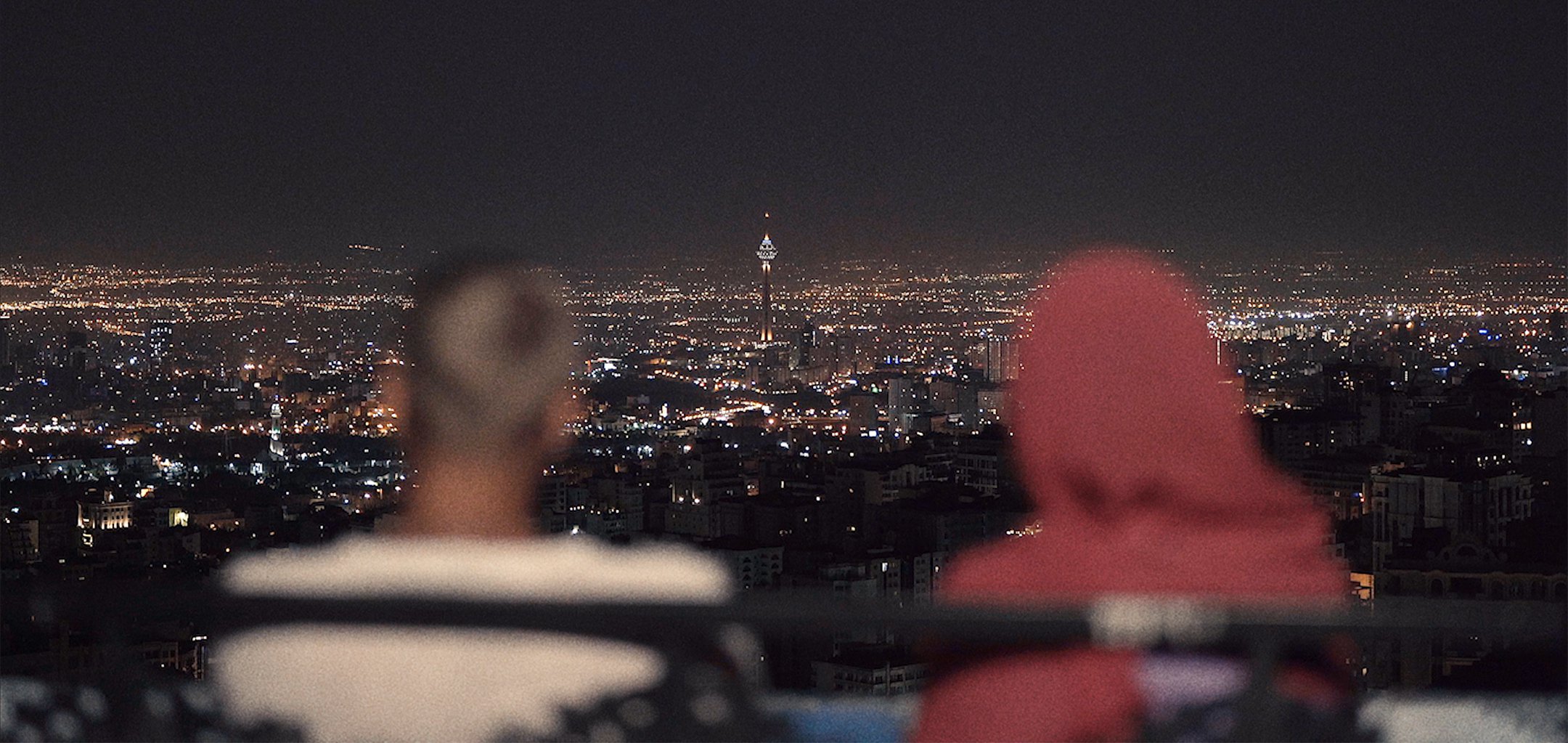 Two figures looking over a cityscape vista at night in 'Happiness' (2021) La Onde Productions