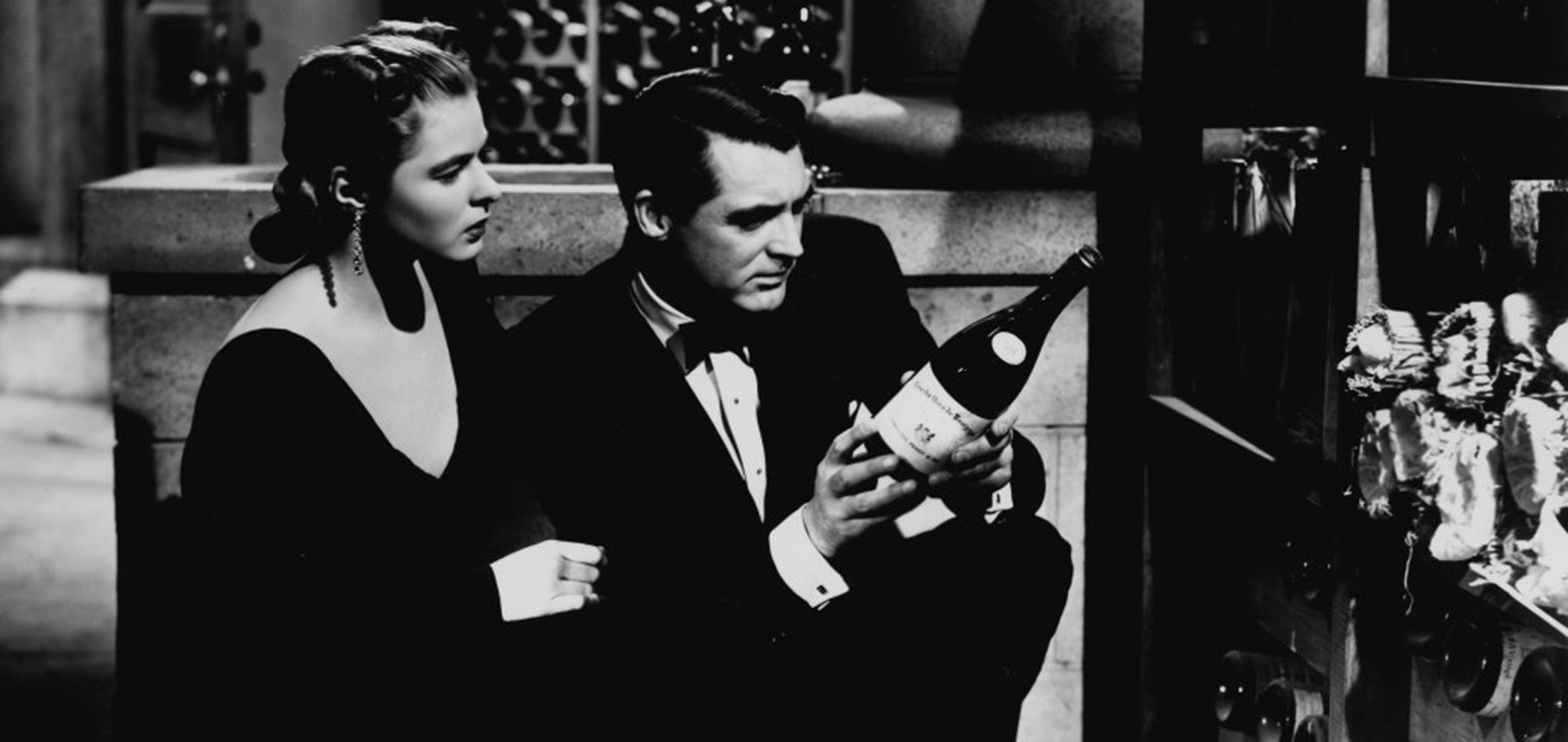 Ingrid Bergman and Cary Grant in formal attire, crouching down to inspect a bottle of wine in 'Notorious' (1946) RKO Radio Pictures