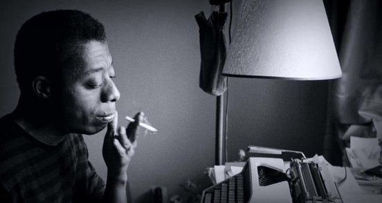James Baldwin smoking and sitting at a typewriter.jpg