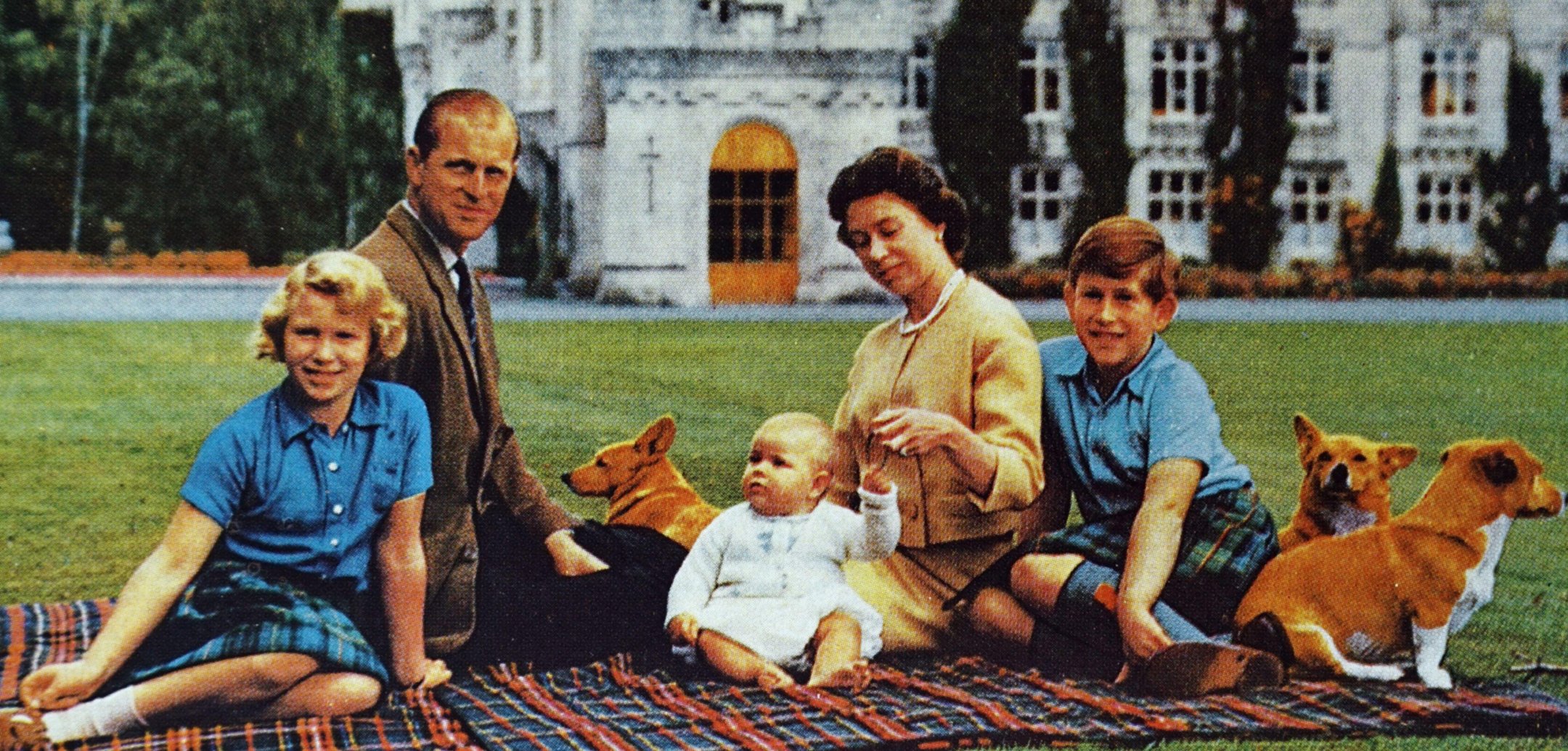 Queen Elizabeth II with the Duke of Edinburgh, their children and corgis at Balmoral Castle. The family is sitting on a picnic rug.