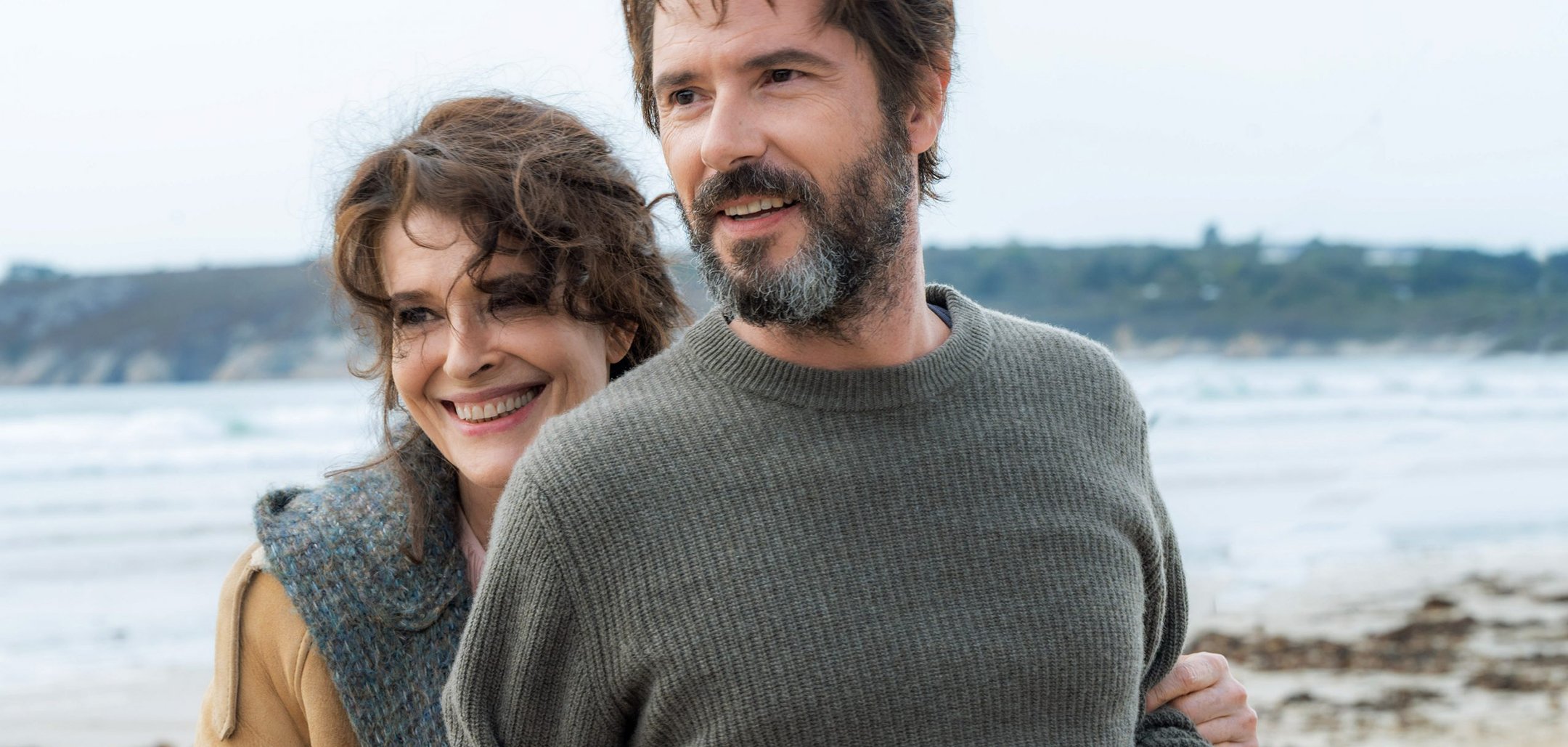 An older woman and a middle aged man smiling on a beach