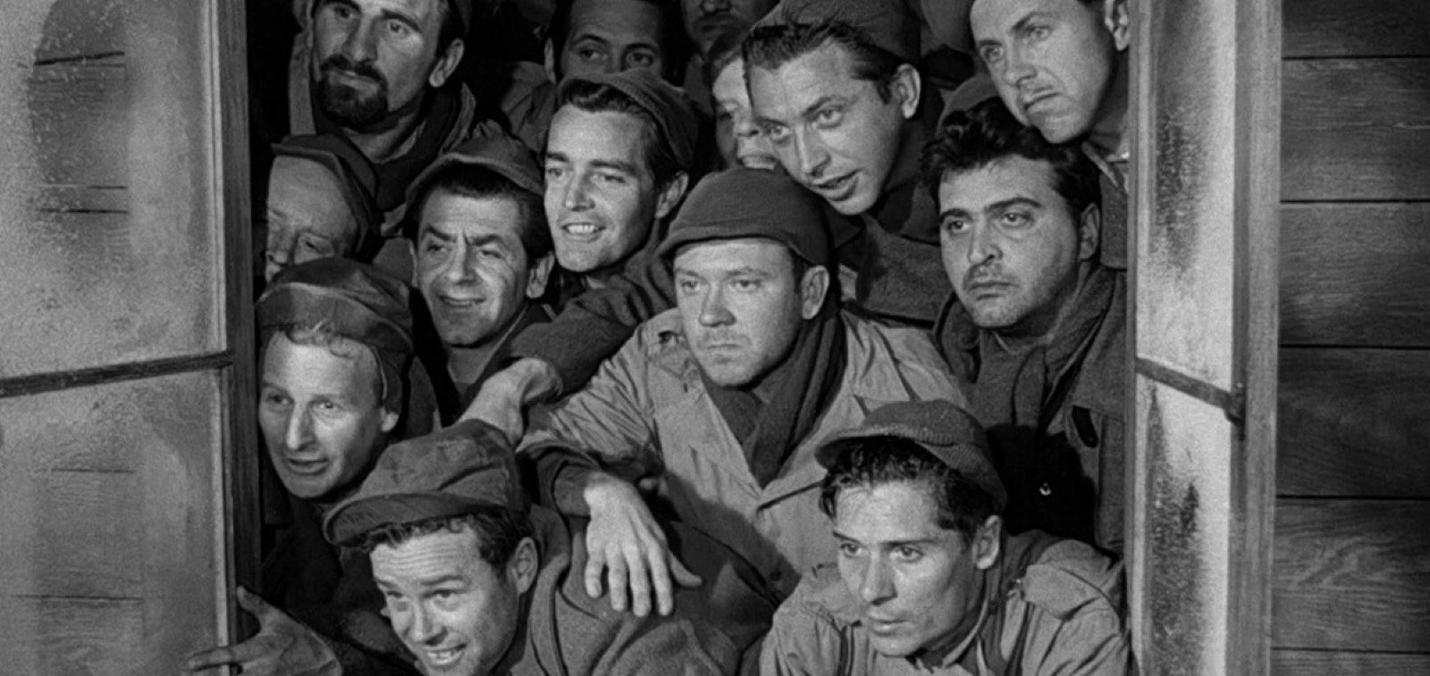 The inmate characters of Stalag 17 crowd together at a window