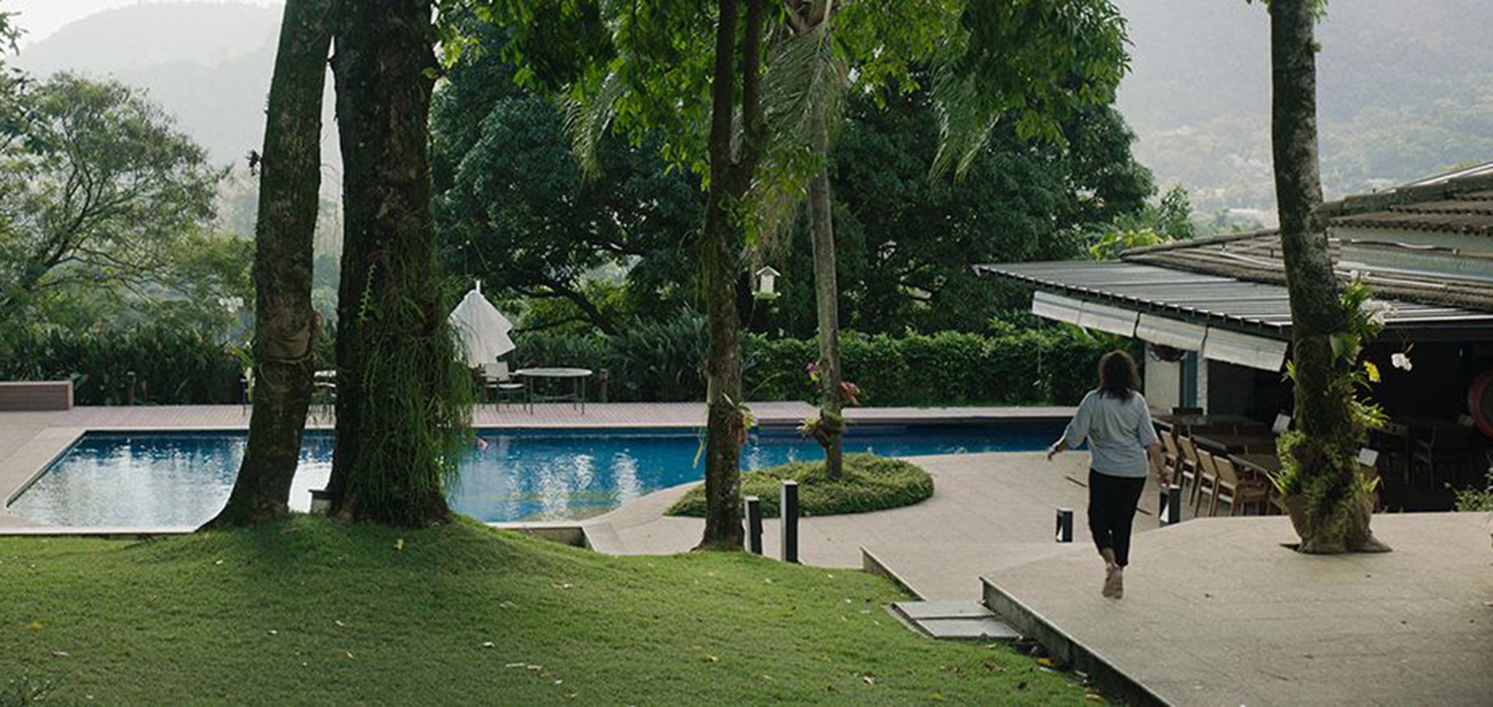 A woman strolling by a backyard pool in an idyllic setting in a still from 'Three Summers' (2019)