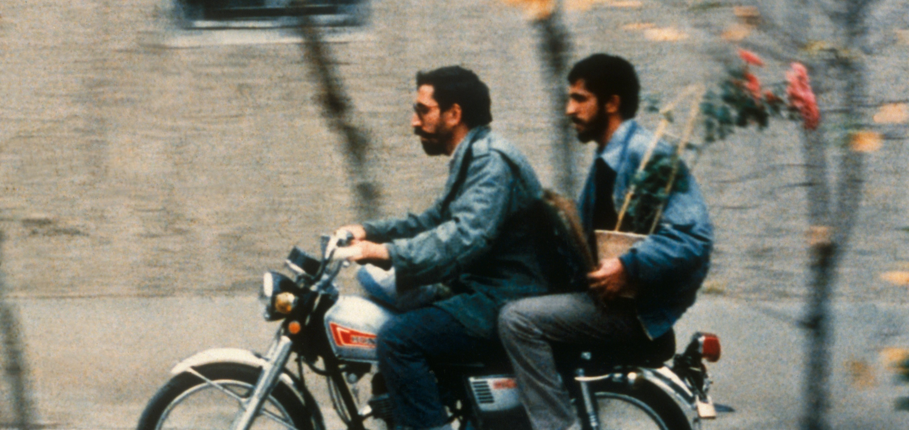 Two men on a motorbike, the one on the back holding a flowerpot in a still from Close-up (1990)
