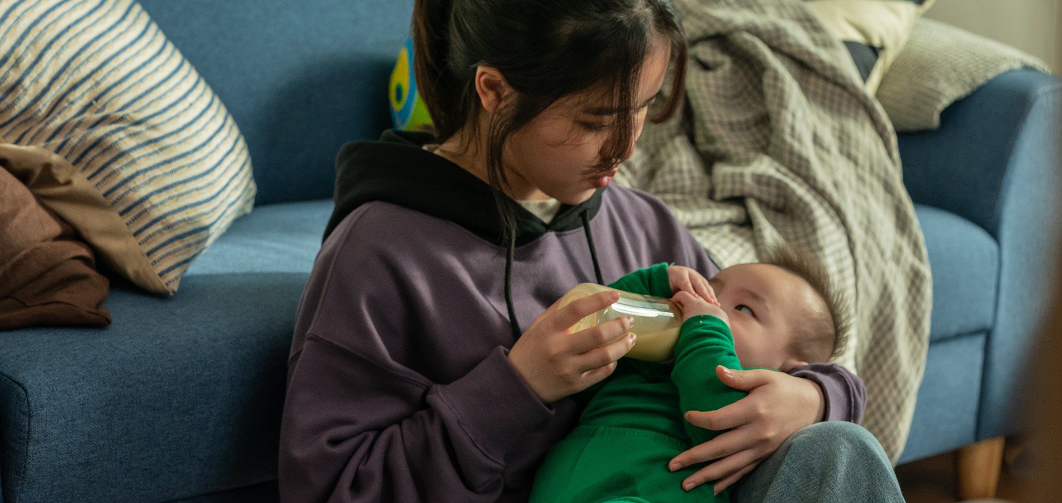 Young woman bottle feeding a baby in a stil from 'I' (2021)
