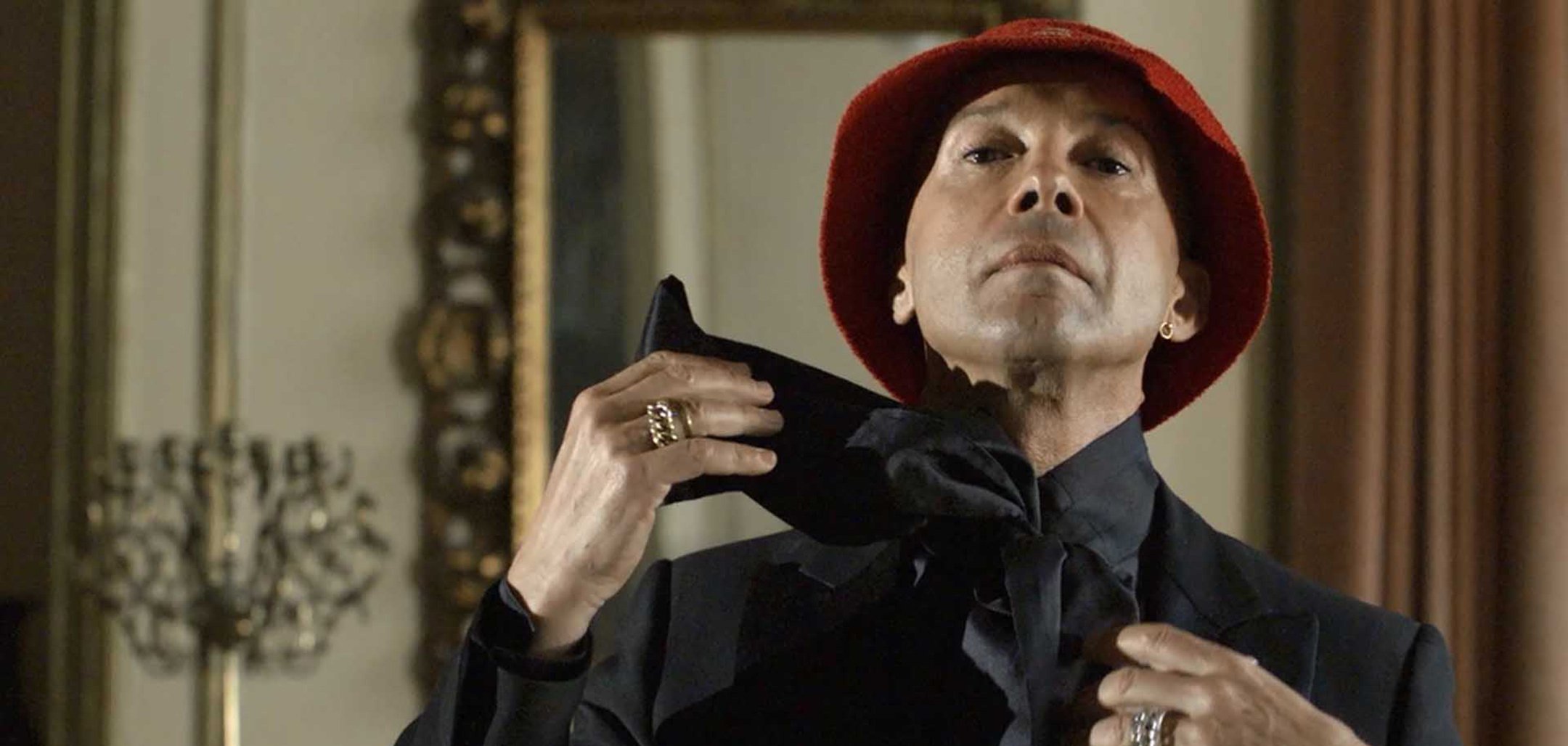 A finely dressed man puts on a scarf in a still from 'Disco Ruin' (2020)