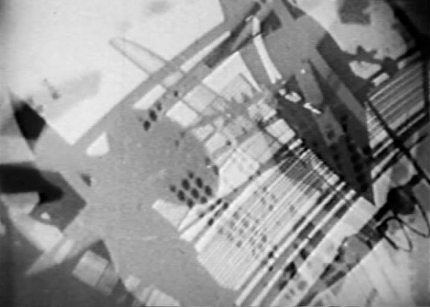 A black and white abstract image of overlapping mechanical shapes, seen through a camera lens
