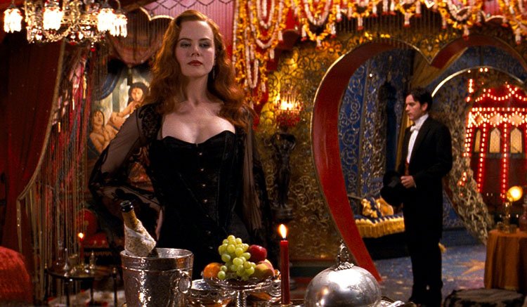 A vibrant image of a red-haired woman, the performer satine from moulin rouge, played by nicole kidman, standing in an elegant gown in a room soaked in warm orange and red light from candles and opulent set dressing