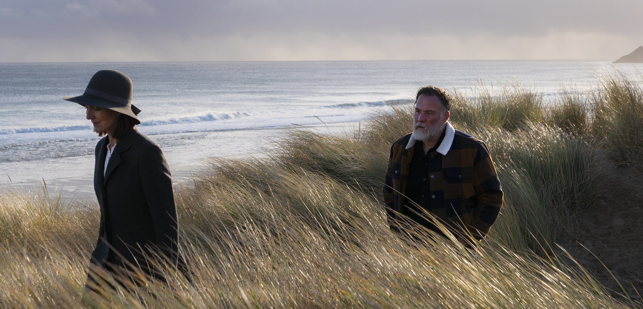 A woman and a man standing in tall grasses along a stormy coastline
