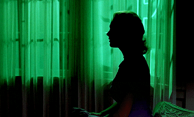 A gif of a woman's silhouette against a deep neon green backdrop, she moves her mouth as if saying something slightly as the camera zooms in.