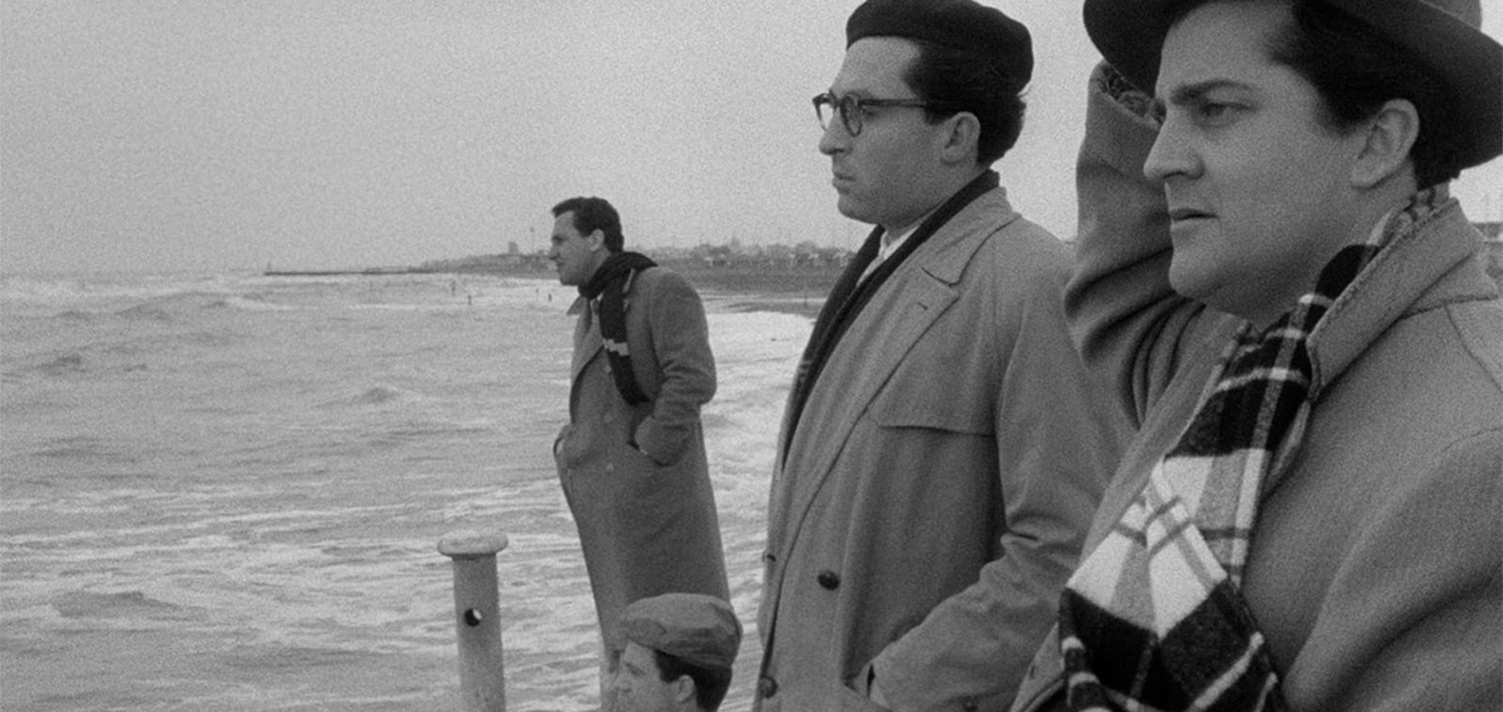 The cast of I Vitelloni (1953) seated at different tables in front of a cafe